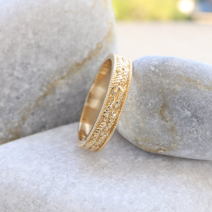 Profile view of a leaf-textured and embossed gold ring resting on a grey stone