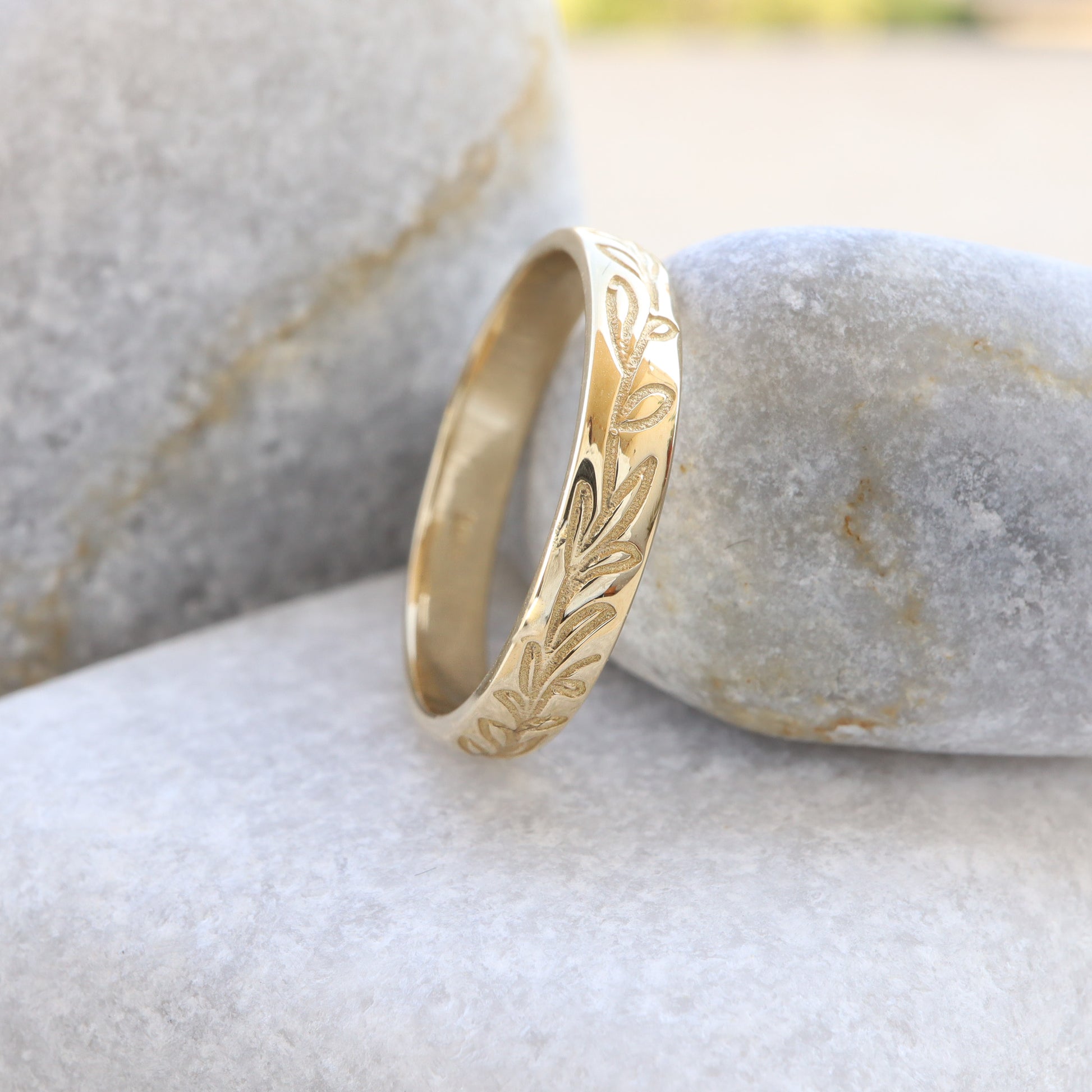 Gold Leaf Wedding Band, resting against a grey rock showing its elegancy