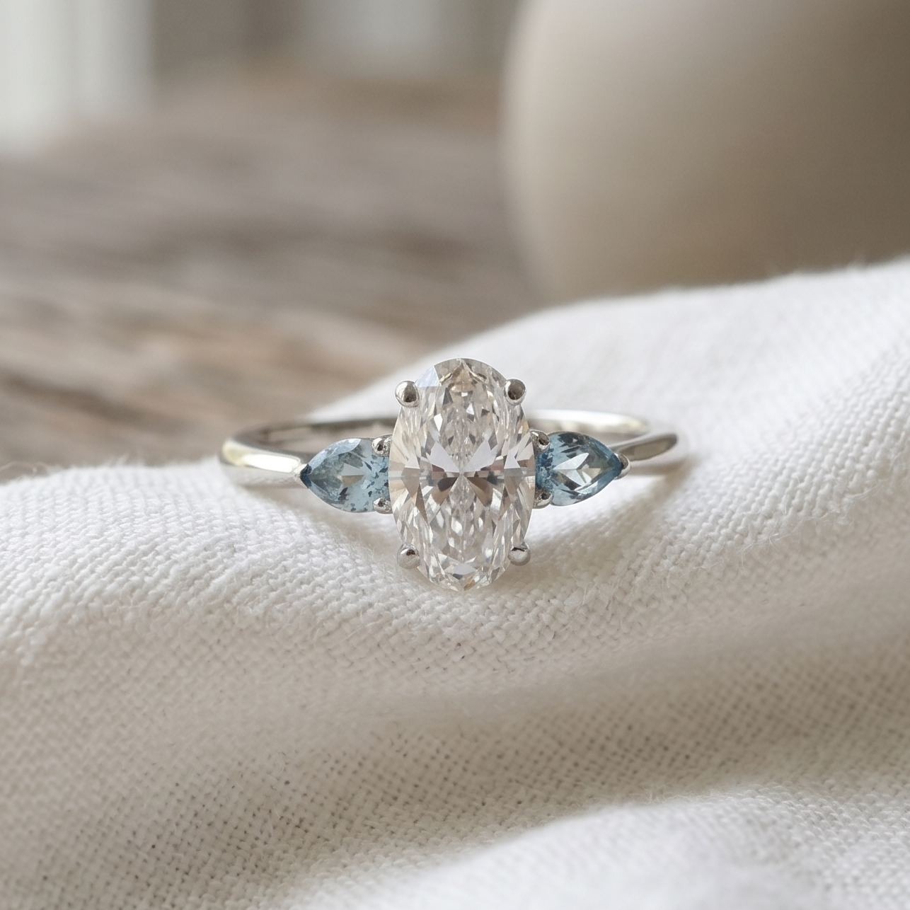 Oval diamond & Light blue aquamarines stones in a white gold three stone design resting on a white linen.