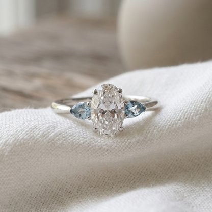 Oval diamond & Light blue aquamarines stones in a white gold three stone design resting on a white linen.
