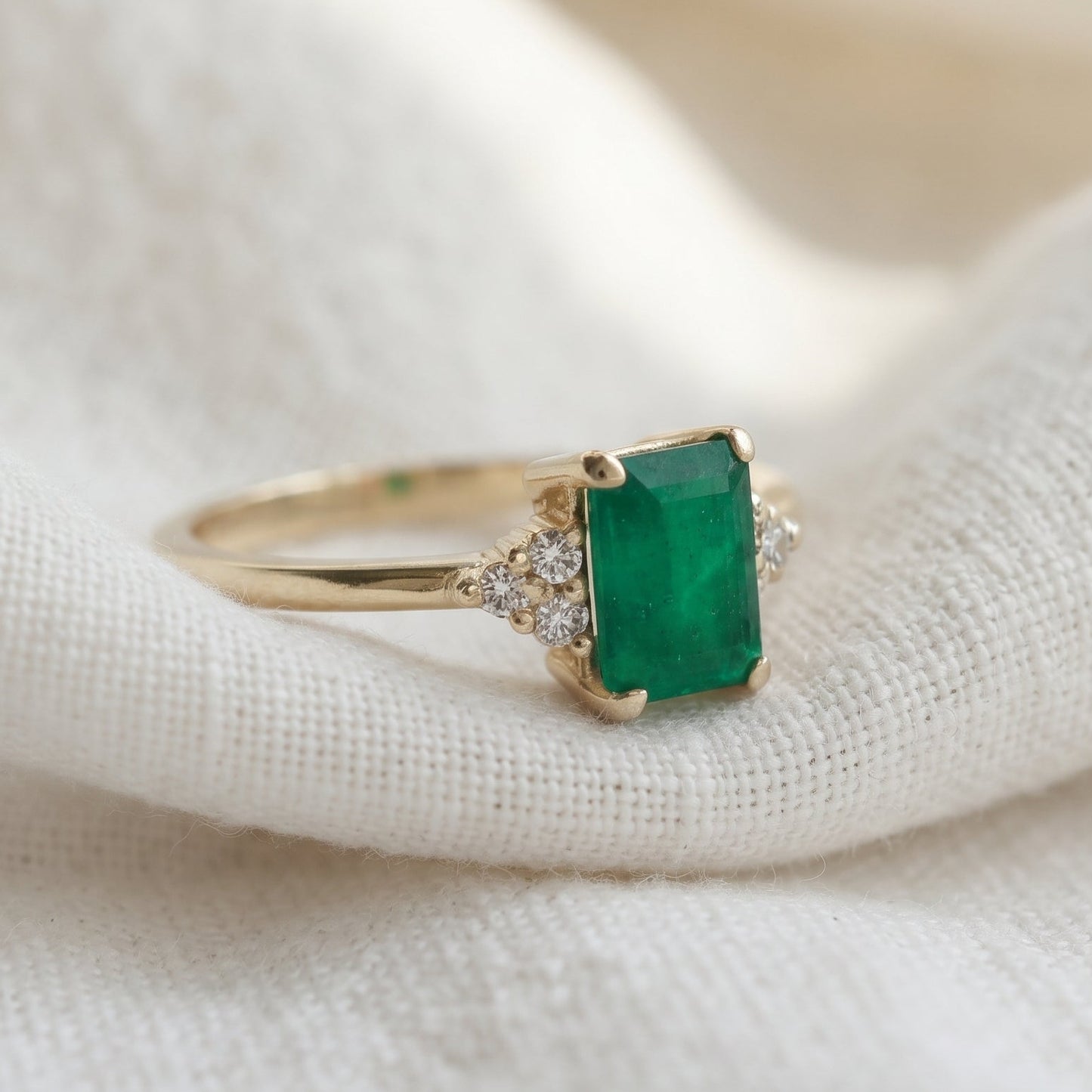 Emerald gemstone in a rectangular shape accented with 3 diamonds on each side.