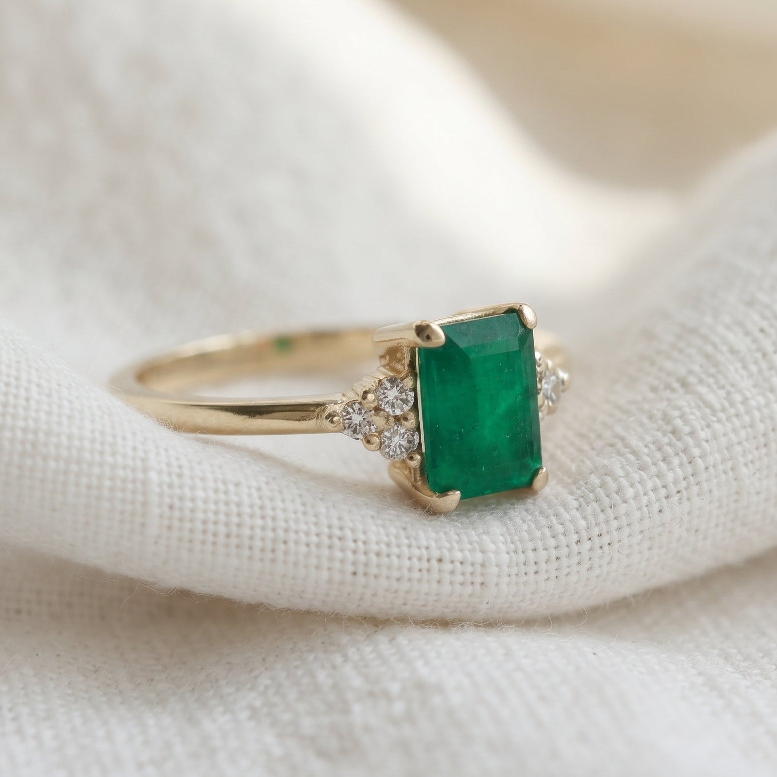Emerald gemstone in a rectangular shape accented with 3 diamonds on each side.