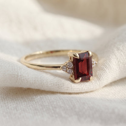 Emerald shape red garnet gemstone ring accreted with 3 diamonds on each side.