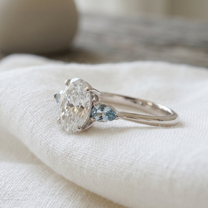 Sideview of a three stone design featuring an oval cut diamond & aquamarines pear shapes.