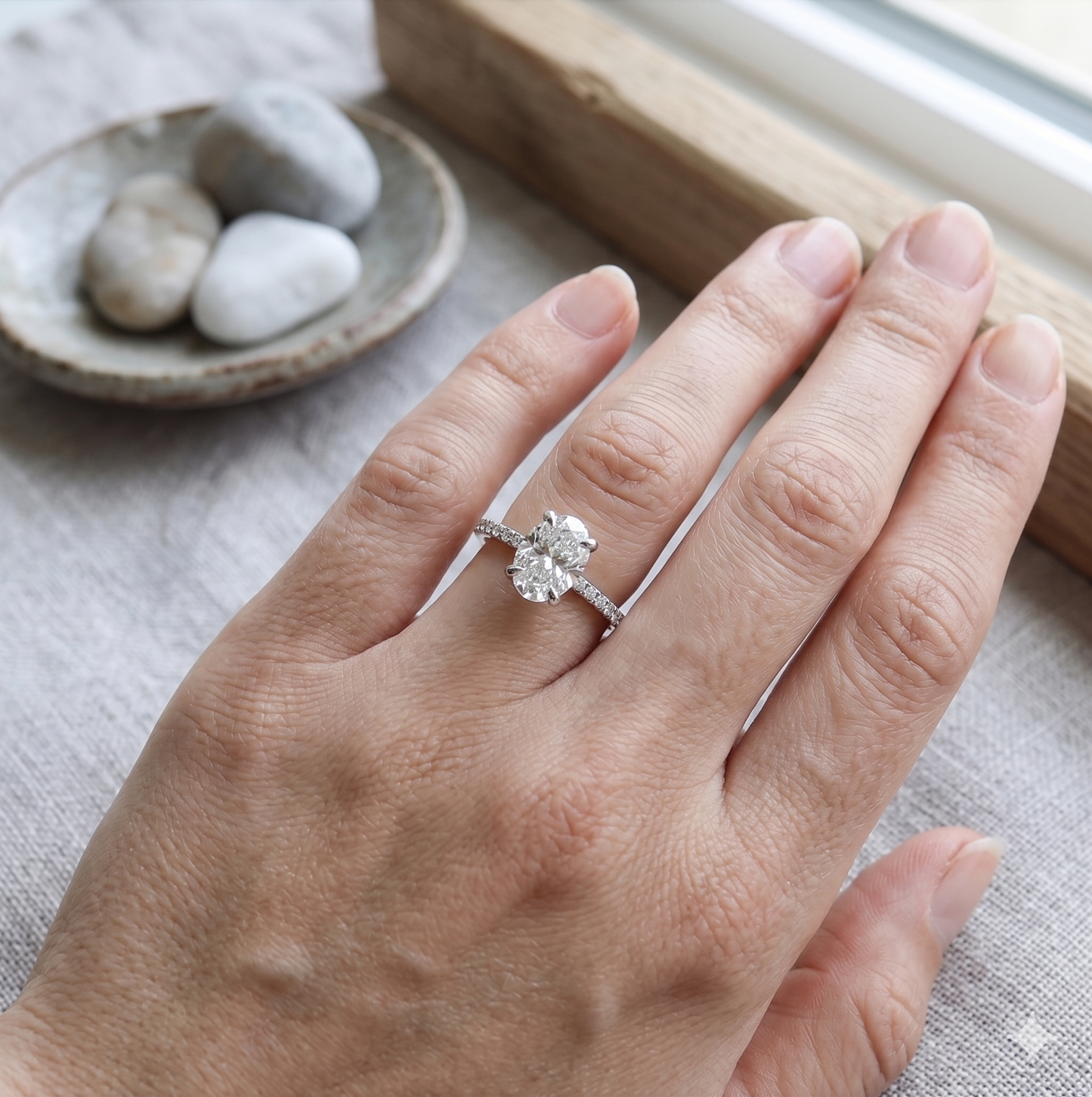 oval diamond ring in white gold with small diamond on the sides on a woman's finger.