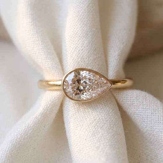 pear shape engagement ring set in an east west bezel setting gold design/