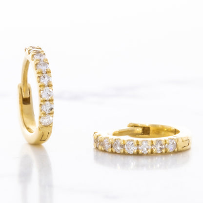 One diamond huggie earring rests open and flat, while the other stands upright, both showcasing their pave setting against a white background