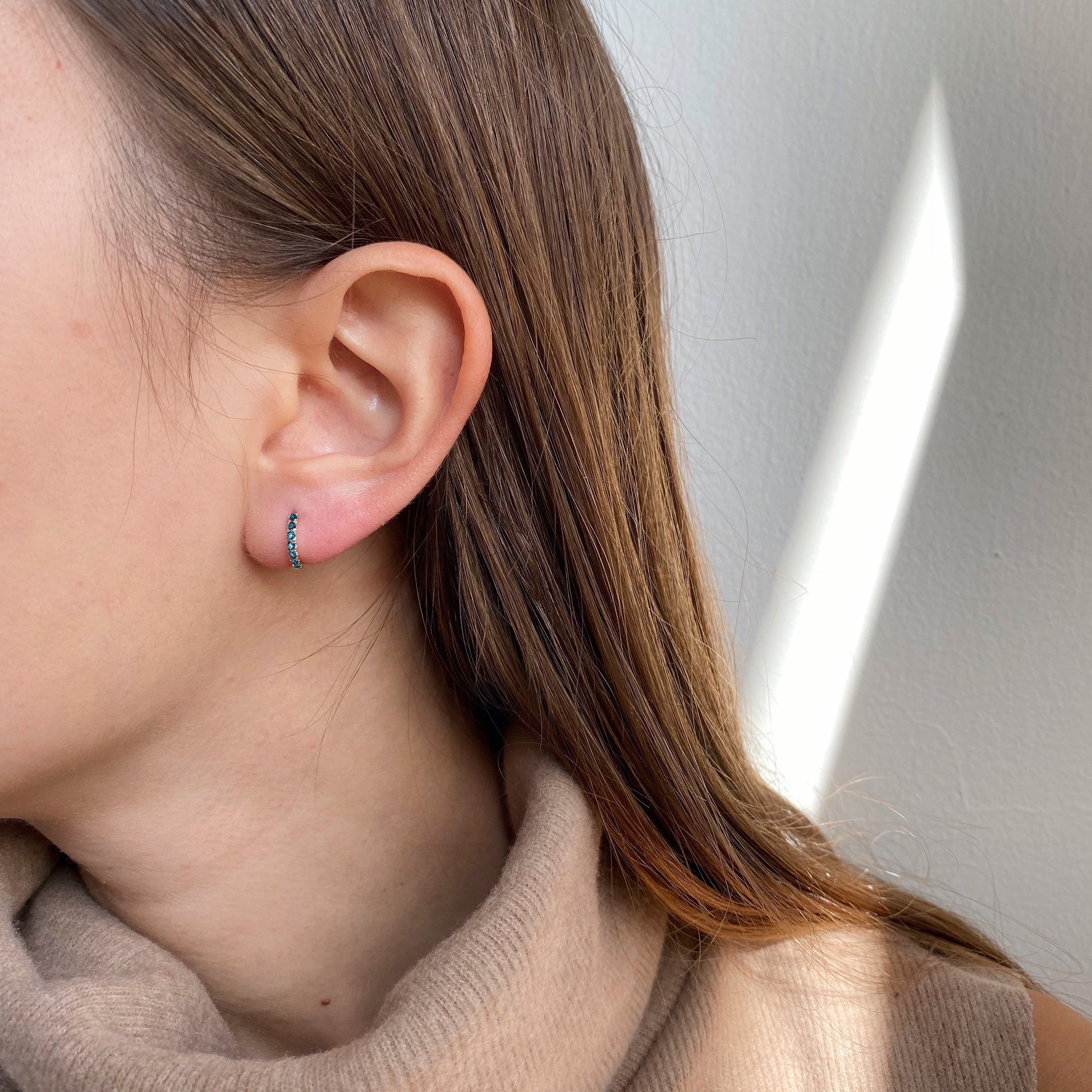 Blue sapphire gold huggie hoop earring, with an elegant pave setting, adorning a woman's ear