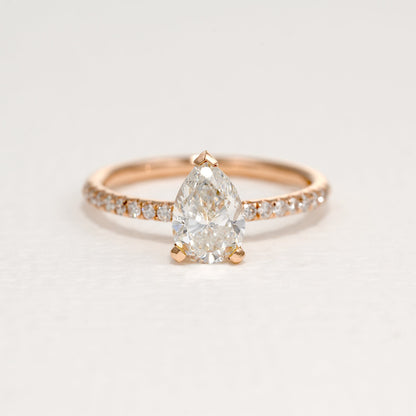 Front view of a pear-shaped diamond set in a two-tone design with round side diamonds, featuring a rose gold band, on a white background