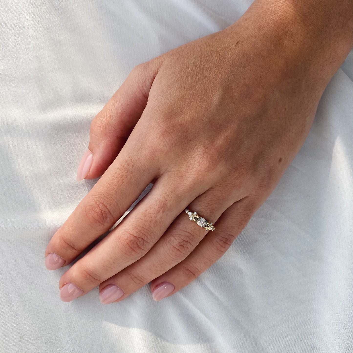 A champagne marquise-cut diamond engagement ring, displayed on a woman's hand, adorned with four small diamonds on either side, inspired by Art Deco