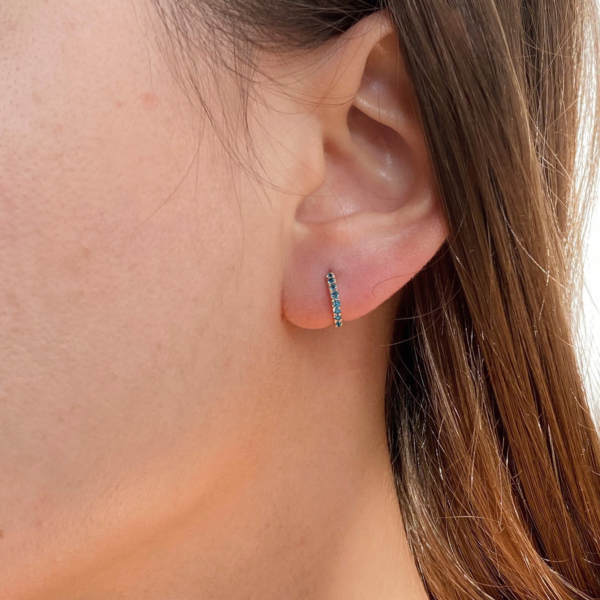 Blue sapphire gold huggie hoop earring in a woman's ear