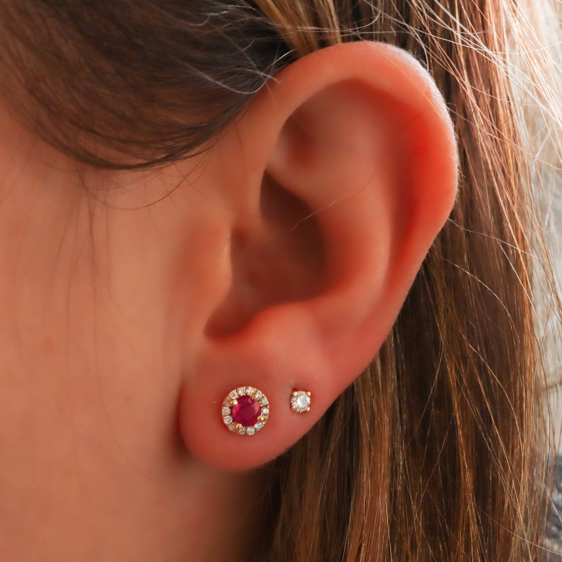 Ruby Halo Stud earring, surrounded by genuine diamonds in gold, gracing a woman's ear, alongside a sparkling diamond stud