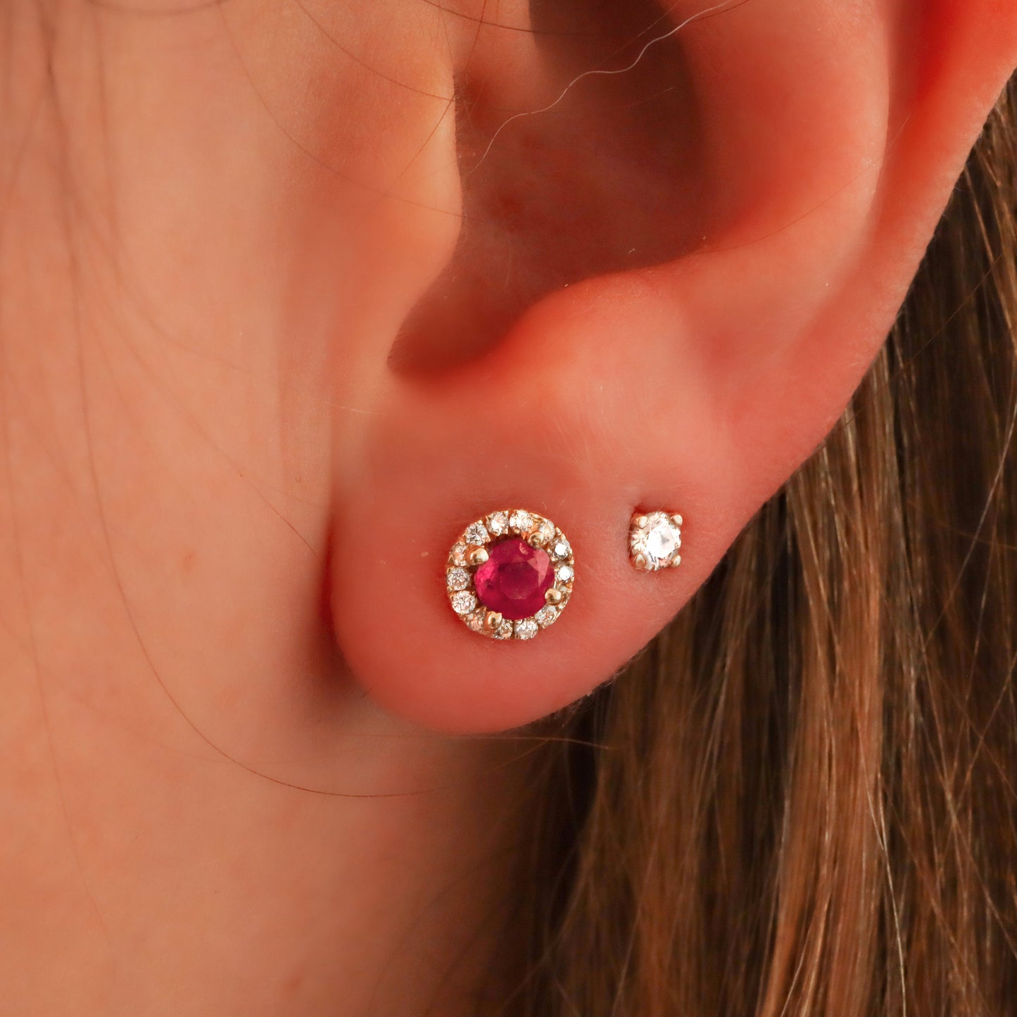 Ruby Halo Stud, encircled by genuine diamonds in gold, on a woman's ear, paired with a diamond stud