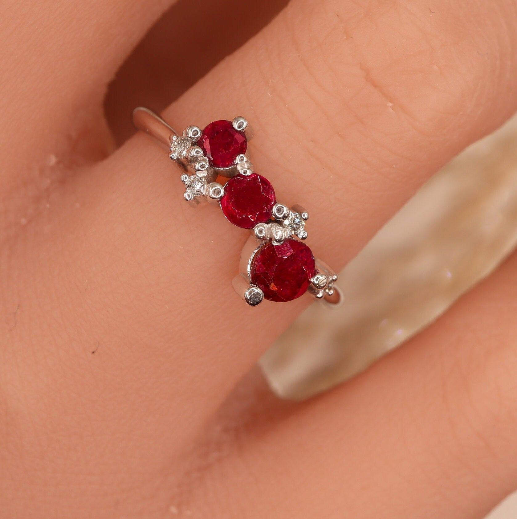 Top view of a woman's hand elegantly adorned with a 3 round Ruby and 4 small round Diamond cluster ring in solid white gold.