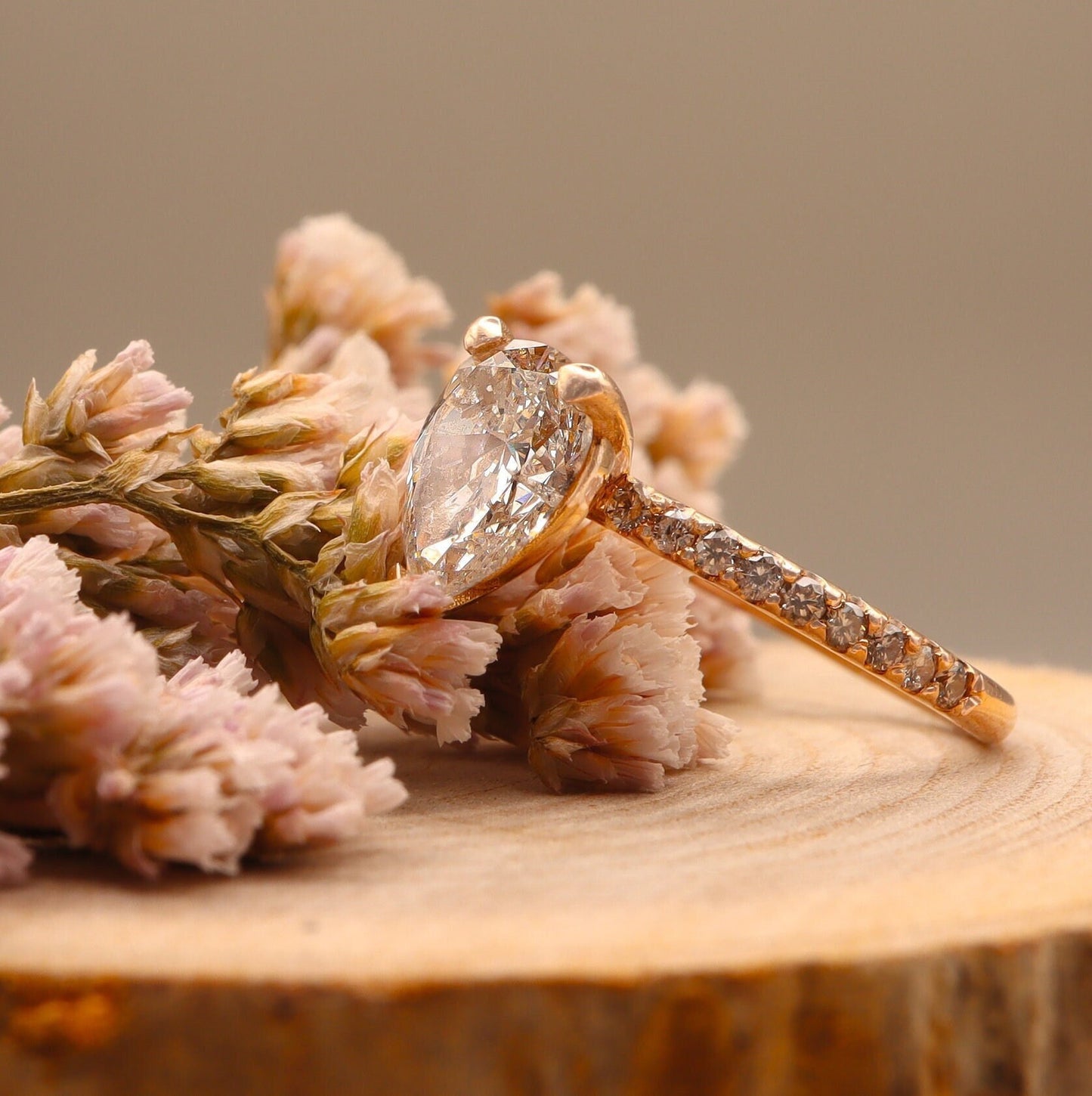 Profile view of a pear-shaped diamond set in a two-tone design with round side diamonds, on a wooden display, featuring a rose gold band