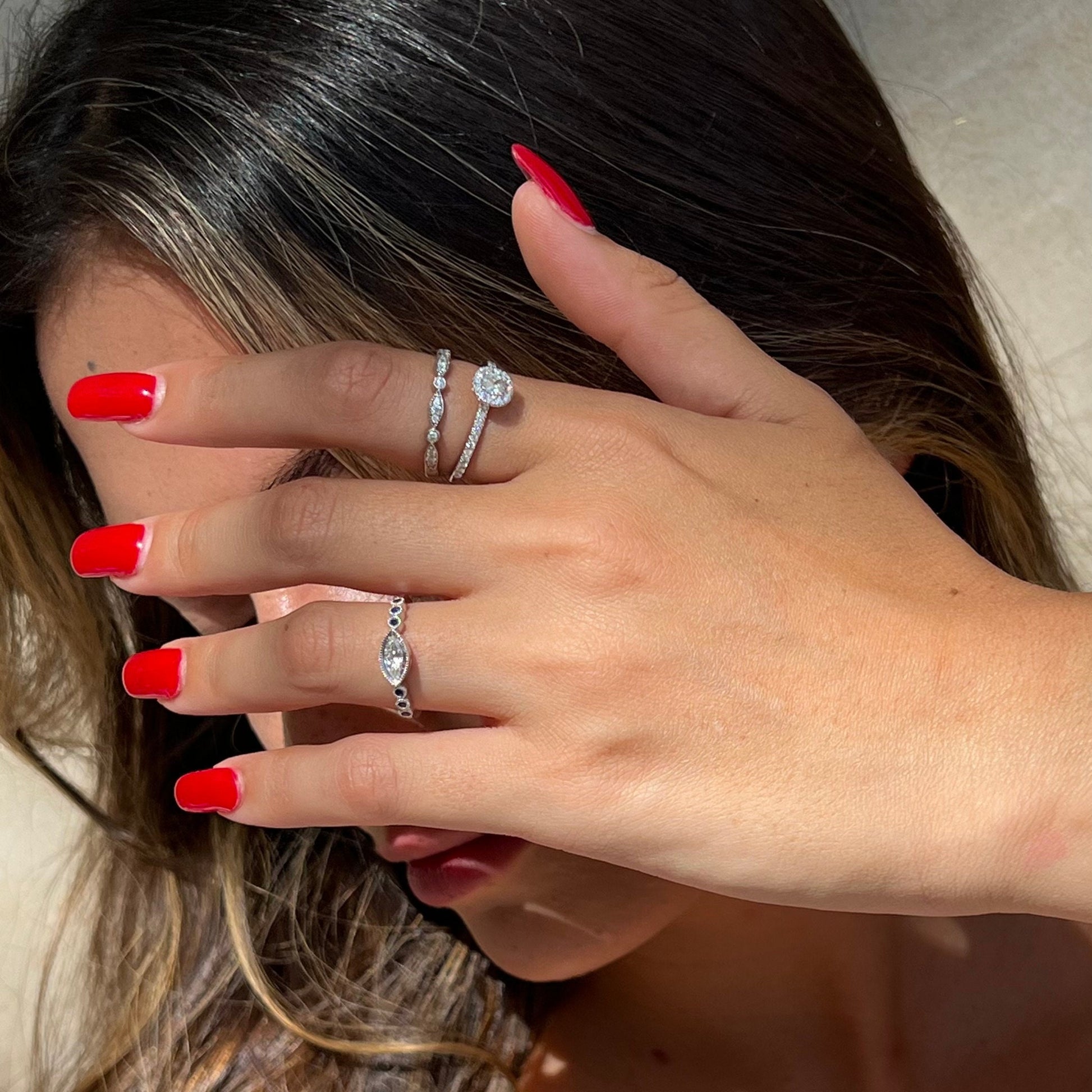 Cushion Cut Diamond Halo White Gold Ring, encircled by natural diamonds, elegantly worn on a woman's hand, accompanied by two other exquisite Dina Jewelry rings