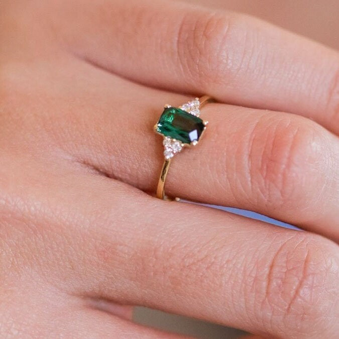 Close-up of a woman's hand wearing a Green Tourmaline Emerald Cut Ring with three small diamonds on each side