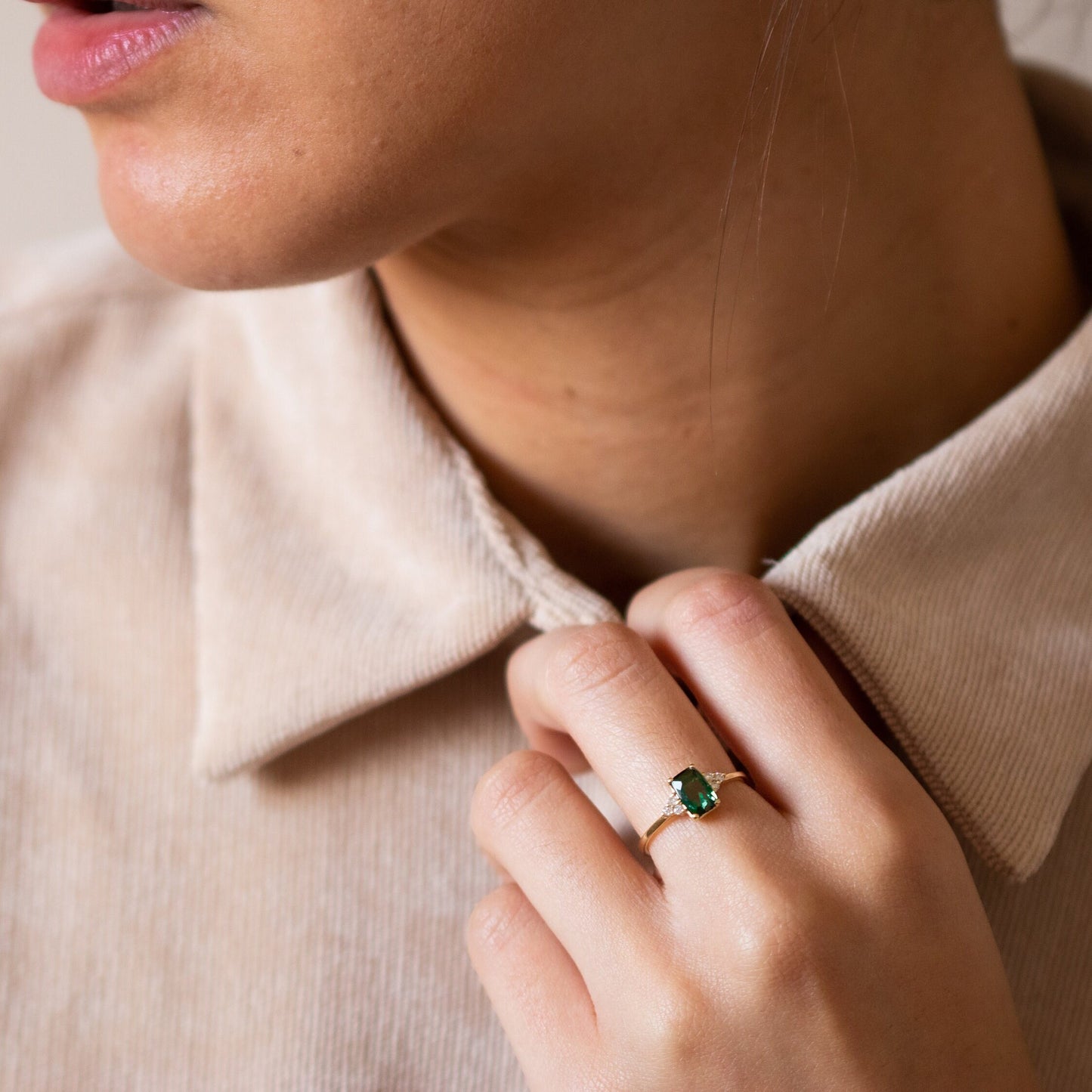 Woman's hand holding her shirt while wearing a Green Tourmaline Emerald Cut Ring with three small diamonds on each side