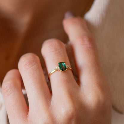 An elegant woman's hand adorned with a Green Tourmaline Emerald Cut Ring featuring three small diamonds on each side.