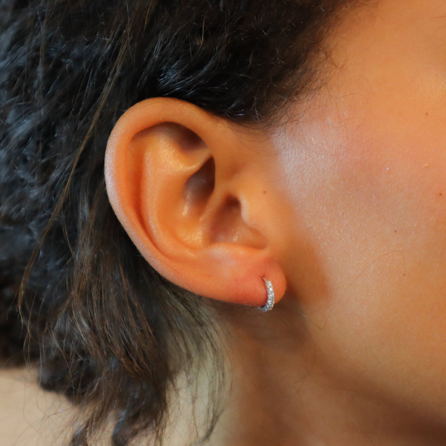 Diamond Huggie Earring, diamonds in a pave setting on a solid white gold hoop, adorning a woman's ear