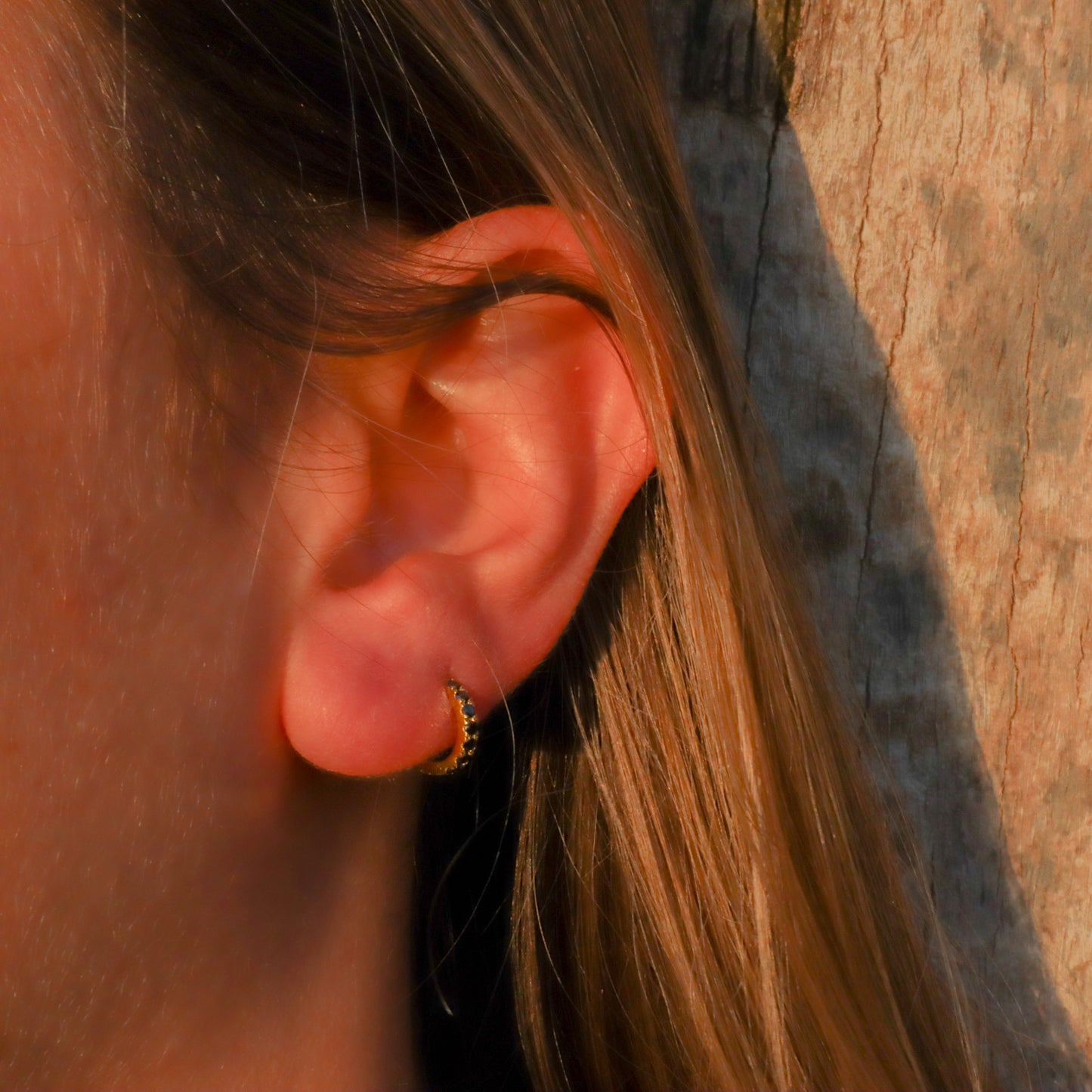 Single black diamond gold huggie hoop earring, elegantly worn in a woman's ear