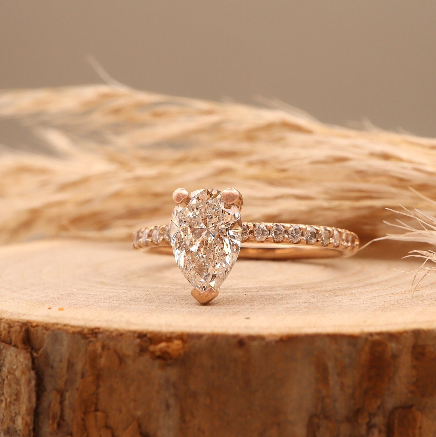 Pear-shaped diamond in a two-tone design with round side diamonds, displayed on a wooden stand