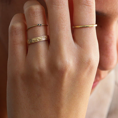 Leaf-textured and embossed gold ring on a woman's hand, accompanied by two other rings from the Dina Jewelry collection."