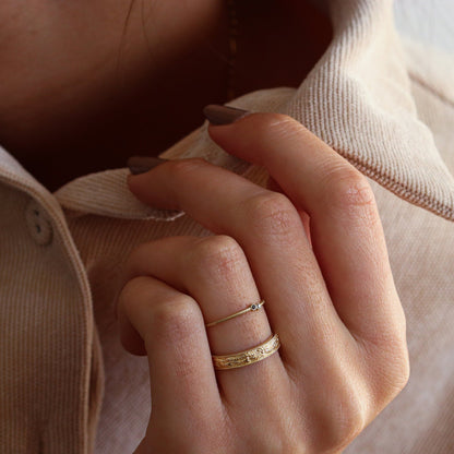 A woman's hand holding her collar, adorned with a leaf-textured and embossed gold ring, alongside one ring from the Dina Jewelry collection