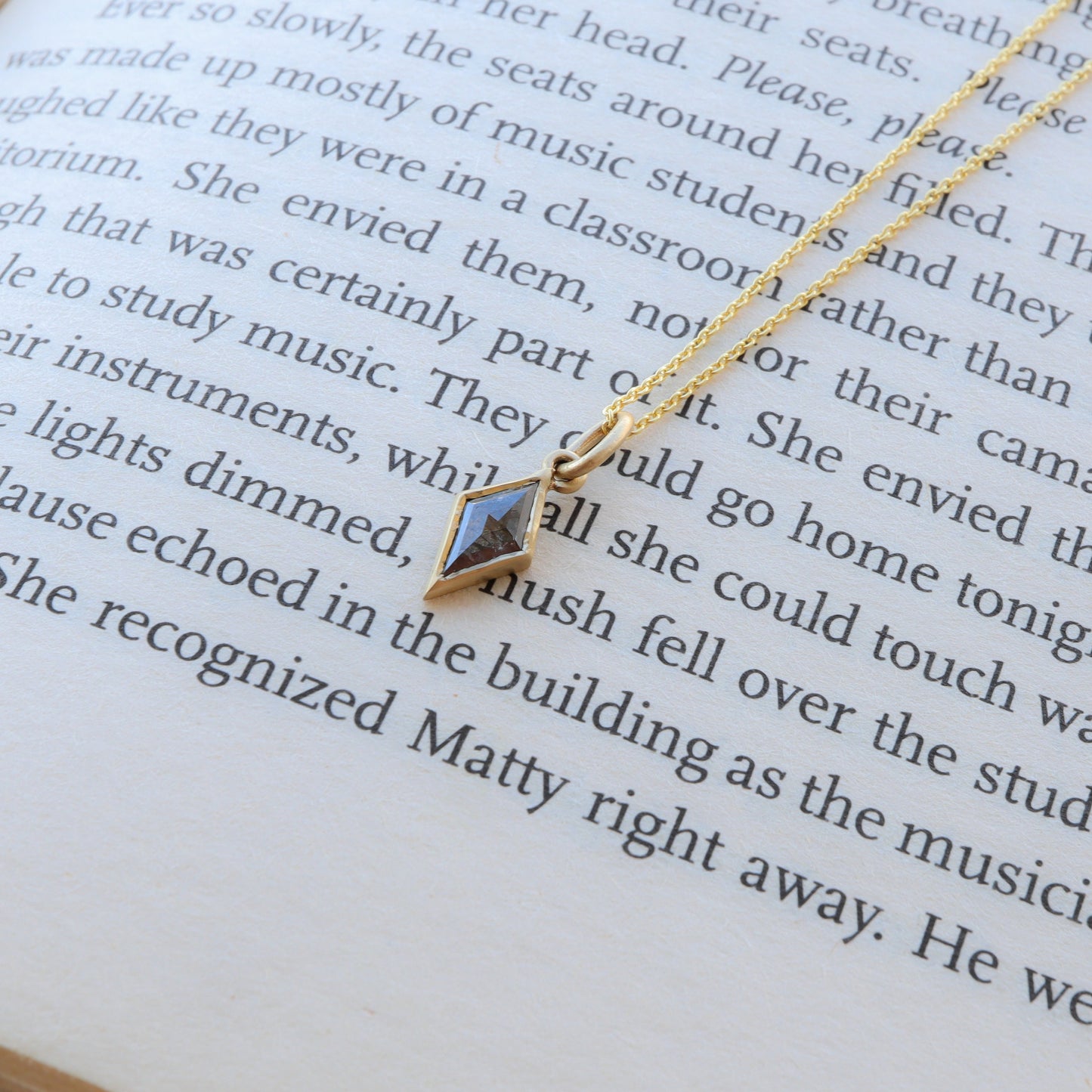 alt and Pepper Diamond Necklace in Kite Shape with Bezel Setting, gleaming in gold, resting in a book