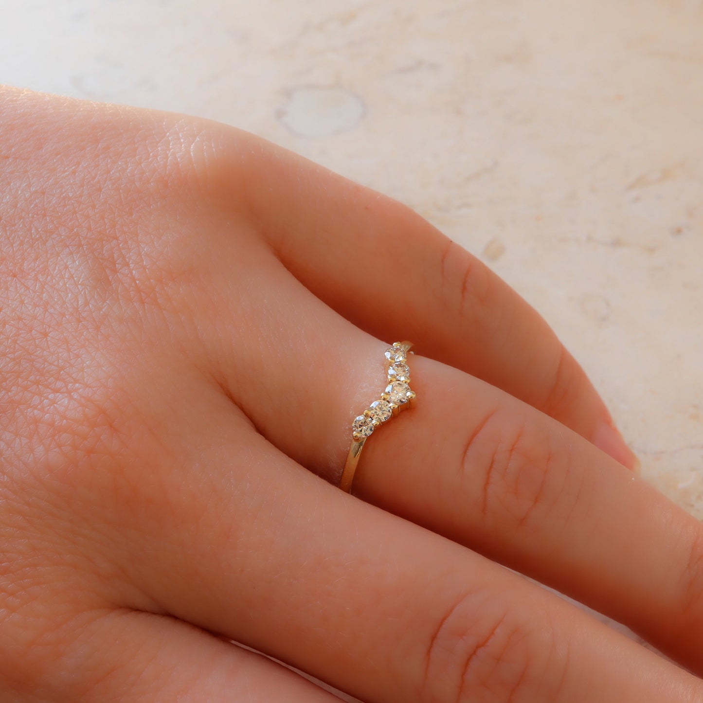 Curved diamond gold ring elegantly adorning a woman's hand on a marble slab