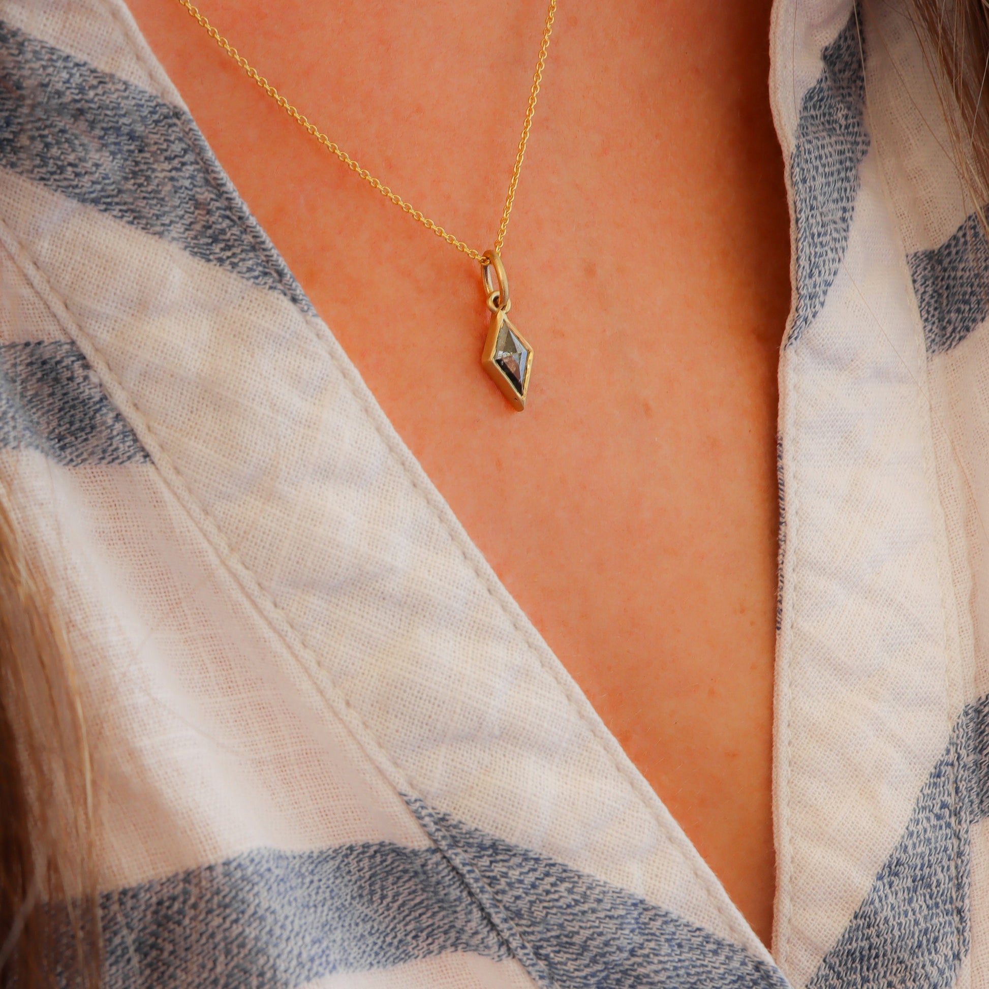 Profile view of Salt and Pepper Diamond Necklace in Kite Shape with Bezel Setting, adorning a woman's neck in a blue and white striped shirt.