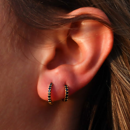 Two black diamond gold huggie hoop earrings gracefully adorning a woman's ear