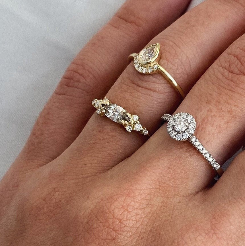 A champagne marquise-cut diamond engagement ring on a woman's hand, accompanied by a white gold halo ring and a pear-bezel ring, all inspired by Art Deco