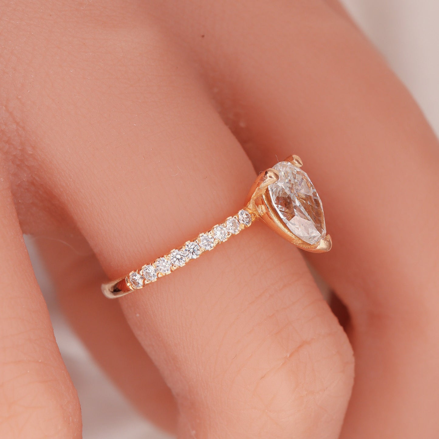 "Profile view of a pear-shaped diamond set in a two-tone design with round side diamonds on a woman's hand, showcasing the rose gold band