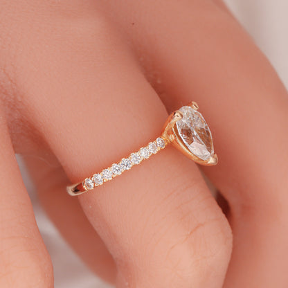 "Profile view of a pear-shaped diamond set in a two-tone design with round side diamonds on a woman's hand, showcasing the rose gold band