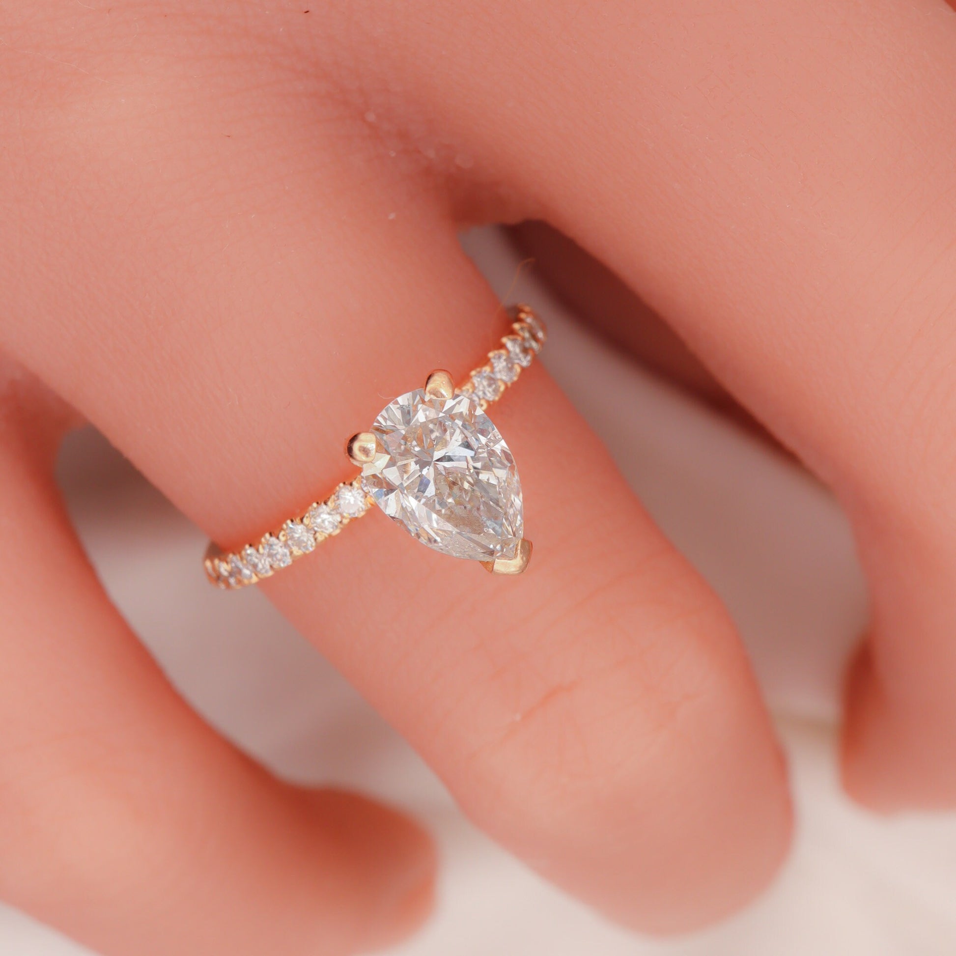 Pear-shaped diamond set in a two-tone design with round side diamonds on a woman's hand, featuring a rose gold band